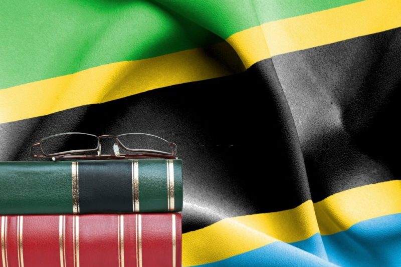 Education concept - Stack of books and reading glasses against National flag of Tanzania